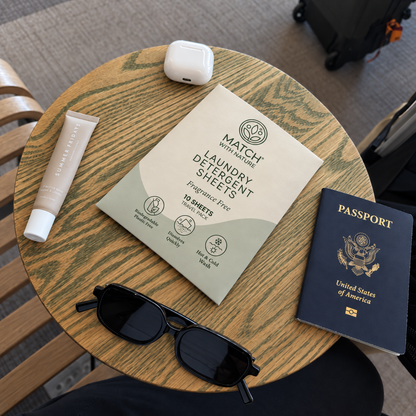 Fragrance Free Travel Pack on a café table at the airport, beside a passport, sunglasses, an earbuds case and lip balm